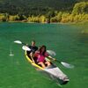 Zwei Personen paddeln in einem aufblasbaren Aqua Marina Kajak Tomahawk AIR-K 14'5" auf einem klaren, türkisfarbenen Gewässer, umgeben von üppiger grüner Landschaft unter einem sonnigen Himmel.