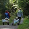 Eckla Atlantica 260 Seekajak-Wagen mit Stütze wird von zwei Personen auf einem schmalen, bewaldeten Weg gezogen, ideal für den Transport von Kajaks zu Gewässern.
