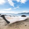 Faltbares Oru Kayak Beach LT auf einem sandigen Ufer, ideal für Freizeitpaddeln auf Seen und Flüssen, zeigt eine helle Farbe mit schwarzen Akzenten in einer ruhigen Naturszene.